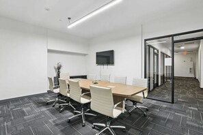 A conference room with a long table, white chairs, a flat-screen TV, and a glass partition wall. - Upscale Downtown 2BR | King + Secured Parking (Birmingham)