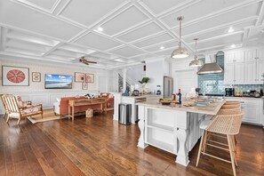 A spacious kitchen with white cabinetry, a large island, and a dining area with a sofa and chairs. - Luxury Pet Friendly Gulf Retreat with Pool + Hot Tub, Game Room and Putting Green | Sleeps 22 (Port Bolivar)