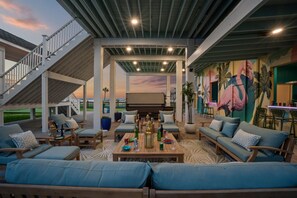 An outdoor living area with multiple seating options, a dining table, and a view of the sunset. - Luxury Pet Friendly Gulf Retreat with Pool + Hot Tub, Game Room and Putting Green | Sleeps 22 (Port Bolivar)