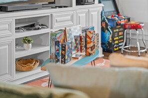 A living room with a TV, shelves, and a table with board games. - Luxury Pet Friendly Gulf Retreat with Pool + Hot Tub, Game Room and Putting Green | Sleeps 22 (Port Bolivar)