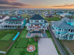 A coastal residential area with multiple houses featuring large porches and a central house with a spacious deck. - Luxury Pet Friendly Gulf Retreat with Pool + Hot Tub, Game Room and Putting Green | Sleeps 22 (Port Bolivar)