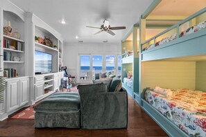 Ein Zimmer mit einem Etagenbett, einem Schreibtisch mit Computer, einem Bücherregal und Blick auf den Ozean.