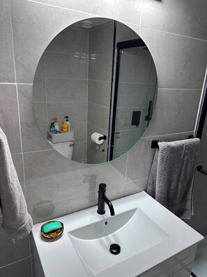 Une salle de bain avec un lavabo blanc, un miroir rond et un porte-serviettes.