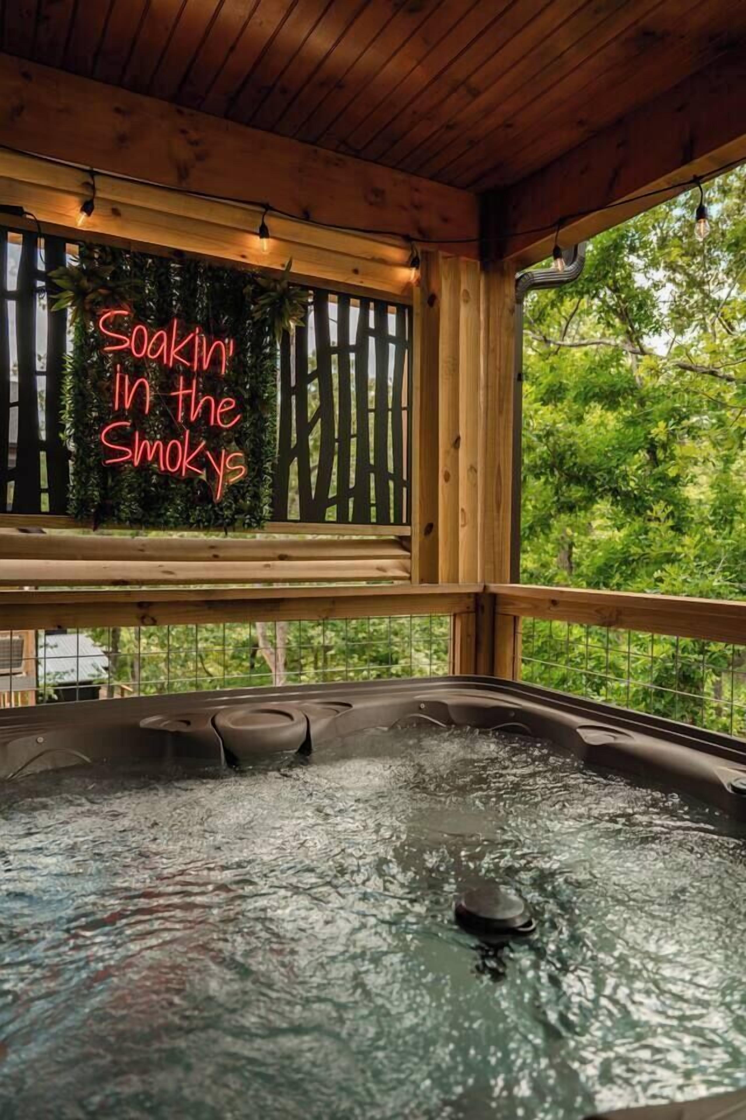 En træhytte med jacuzzi og et neonskilt der står 'Soakin' in the Smokys'.