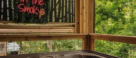 A wooden cabin with a hot tub and a neon sign that reads 'Soakin' in the Smokys'.