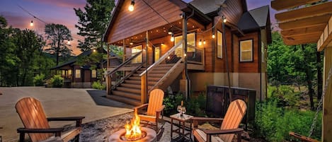 Una cabaña de madera con chimenea, asientos exteriores y una escalera que lleva a un nivel superior.