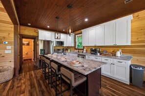 A modern kitchen with white cabinets, a granite countertop, and a central island with bar stools. - Heated Pool, 2 Firepits, Game Room, Theater, 3200 SQFT (Sevierville)