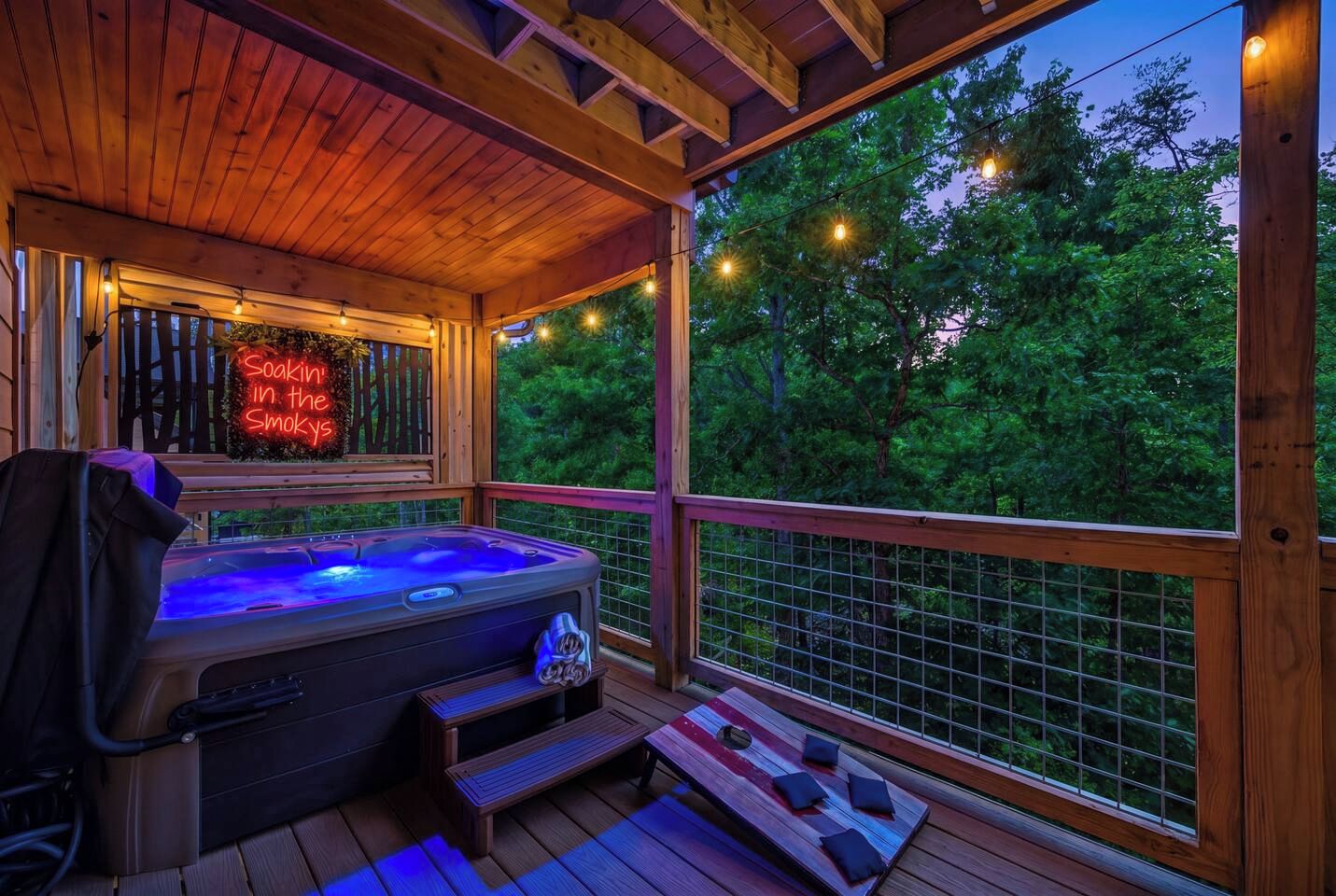 Una terraza de madera con un jacuzzi, un letrero de neón y vistas a árboles.