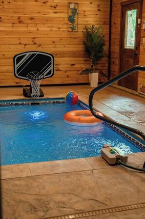 An indoor pool with a basketball hoop, a blue and red ball, and an inflatable ring. - Heated Pool, 2 Firepits, Game Room, Theater, 3200 SQFT (Sevierville)