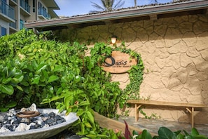 A stone wall with a wooden sign reading 'Oasis on the beach,' a wooden bench, and a fire pit with rocks. - Waipouli Beach Resort H303 Ocean View 2 BD 3 BA (Kapaa)