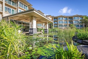 A hotel with a pool surrounded by water lilies and tropical plants, a covered entrance, and multiple balconies. - Waipouli Beach Resort H303 Ocean View 2BD/3BA SEPT/OCT SPECIAL (Kapaa)