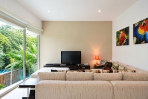 A modern living room with a large sofa, a flat-screen TV, and a dining table.