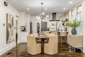 A modern kitchen with white cabinetry, a central island, and a dining area with a round table and chairs. - Luxury Designer Suite 2BR• Boston • Sunroom (Boston)