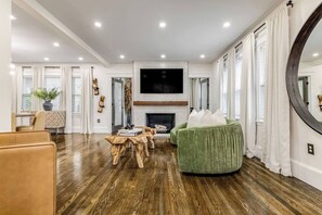 A spacious living room with a fireplace, a large flat-screen TV, and a green armchair. - Luxury Designer Suite 2BR• Boston • Sunroom (Boston)