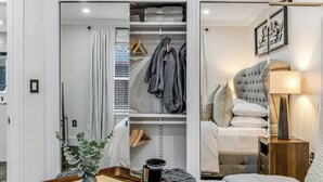 A modern bedroom with a bed, bedside table, lamp, and a view of a closet with hanging clothes. - Luxury Designer Suite 2BR• Boston • Sunroom (Boston)