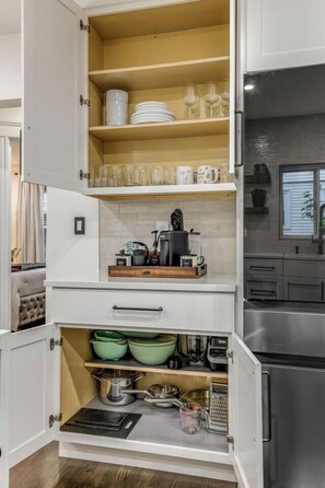 A kitchen with open cabinets displaying dishes, glasses, and kitchenware. - Luxury Designer Suite 2BR• Boston • Sunroom (Boston)
