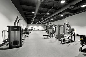 Ein Fitnessraum mit verschiedenen Trainingsgeräten, Bänken und einer hohen Decke mit Beleuchtung.