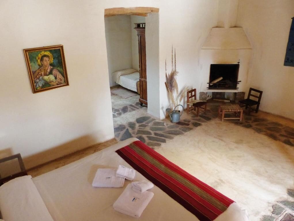 Una habitación con cama, chimenea, un cuadro y suelo de piedra.
