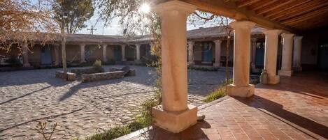 A courtyard with stone flooring, columns, and a covered area with a wooden ceiling.