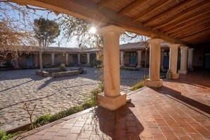 Un patio con suelo de piedra, columnas y una zona cubierta con techo de madera.