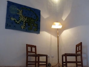 A room with two wooden chairs, a wall-mounted lamp, and a painting of a dinosaur.