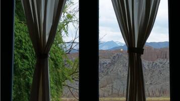 Vista a través de cortinas de un paisaje montañoso con árboles y cielo despejado.