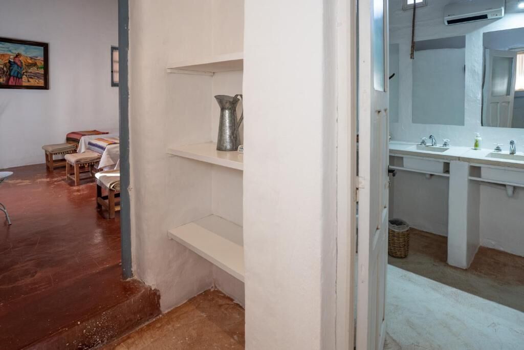 A bathroom with a large mirror, two sinks, and a shelf with a metal pitcher.
