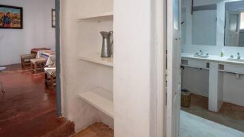 A bathroom with a large mirror, two sinks, and a shelf with a metal pitcher.