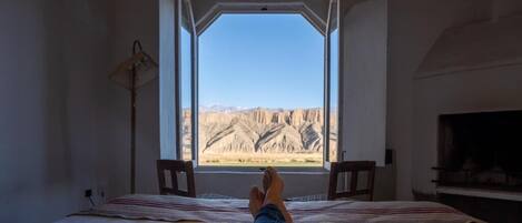 Una cama con vistas a un paisaje montañoso a través de una ventana abierta.