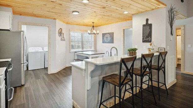 Cocina moderna con techo de madera, muebles blancos y una barra con taburetes.