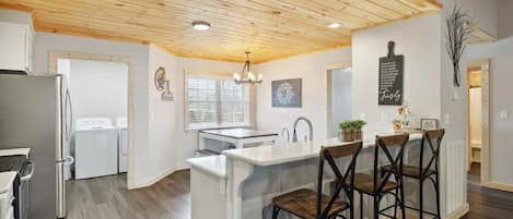 Een moderne keuken met houten plafond, witte kasten en een bar voorzien van krukjes.