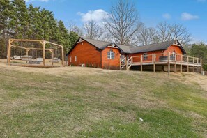 Eine Holzblockhütte mit einer Terrasse und einer Schaukel in einer grünen Wiese.