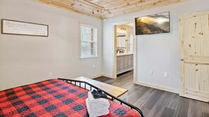 Un dormitorio con cama, ventilador de techo, ventana, baño con lavamanos y puerta.