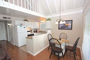A modern kitchen with white cabinetry, a central island, and a dining area with two chairs and a glass table. - Viewcatcher: Gatlinburg 2BR A-Frame Cabin w/ Mountain Views, Hot Tub & Resort Pools (Gatlinburg)