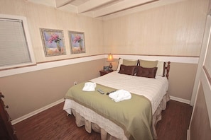 A hotel room with a bed, two paintings on the wall, a nightstand, and a lamp. - Viewcatcher: Gatlinburg 2BR A-Frame Cabin w/ Mountain Views, Hot Tub & Resort Pools (Gatlinburg)