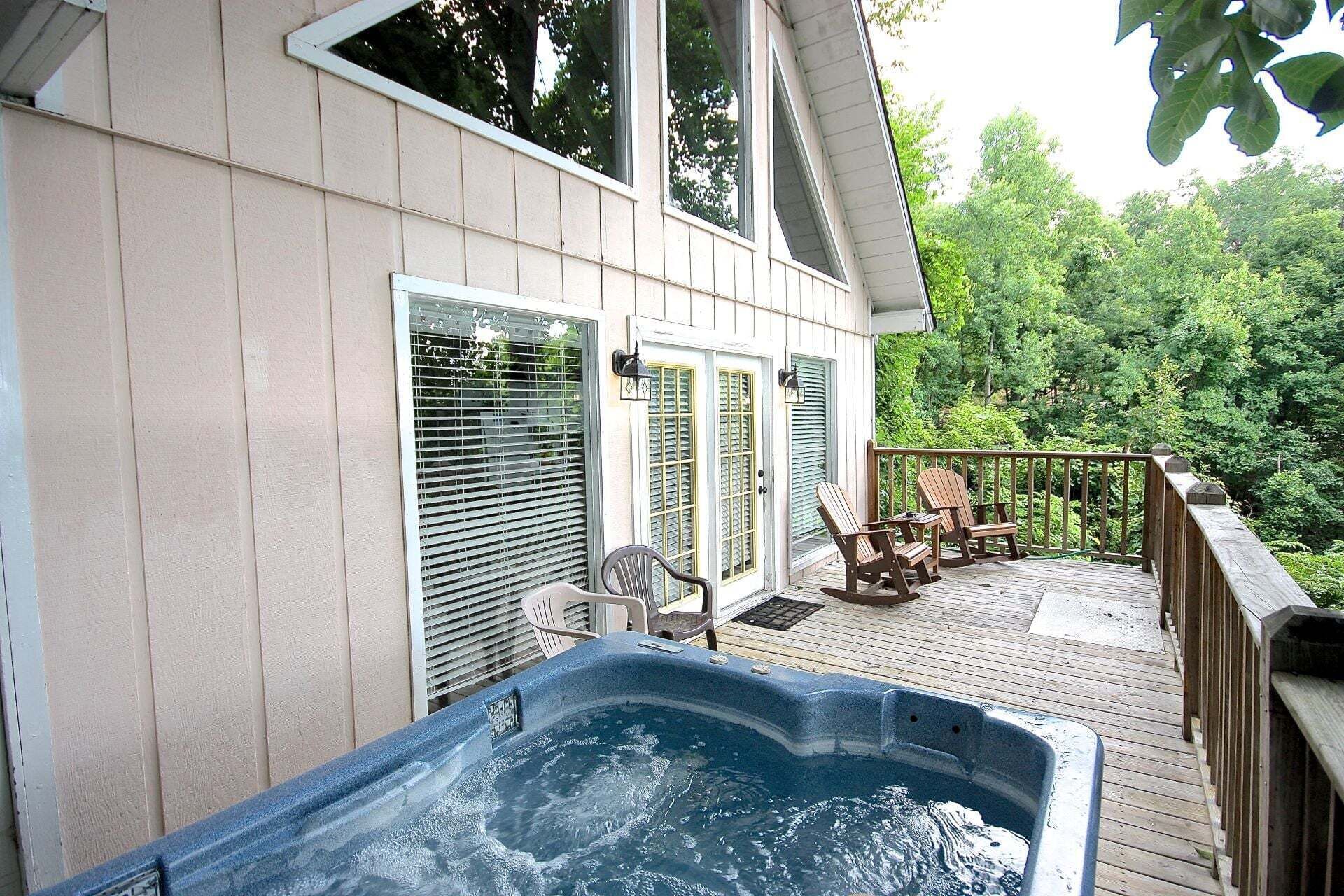 Eine Terrasse mit Whirlpool, Sitzgelegenheiten im Freien und Blick auf einen Wald.