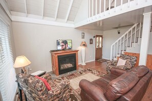 A living room with a fireplace, a television, a patterned sofa, and a staircase. - Viewcatcher: Gatlinburg 2BR A-Frame Cabin w/ Mountain Views, Hot Tub & Resort Pools (Gatlinburg)