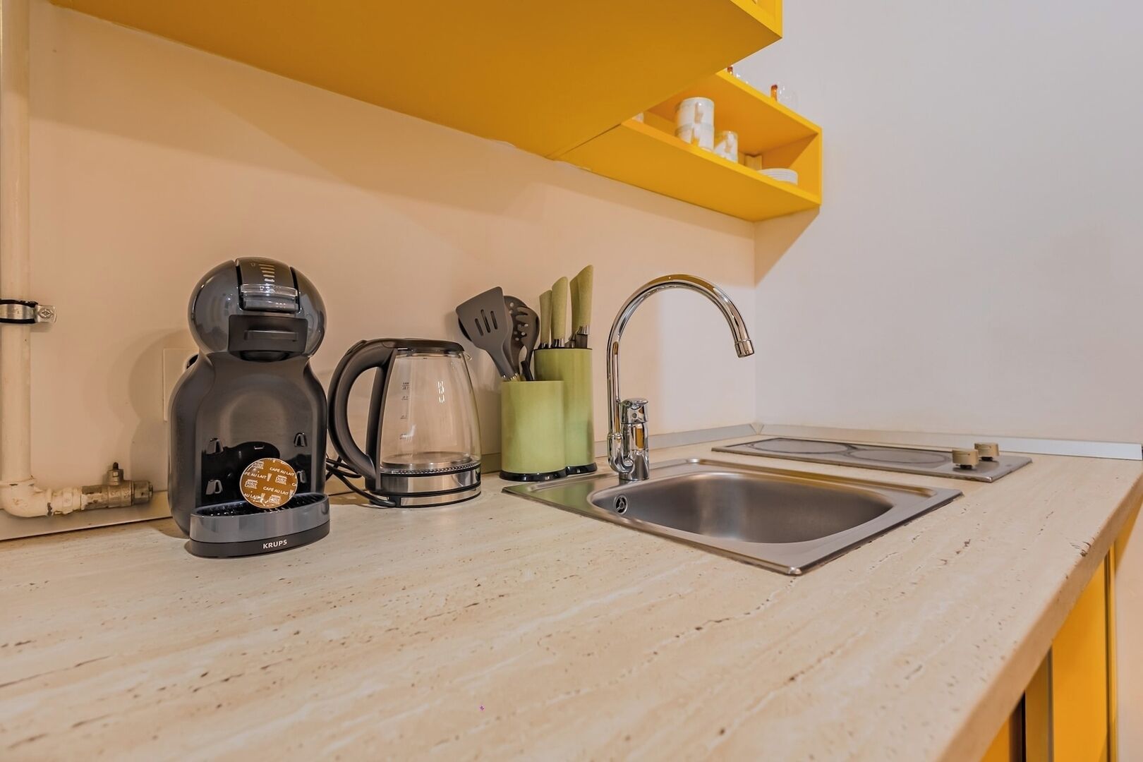 Una cocina con cafetera, hervidor, pileta y un organizador de utensilios.