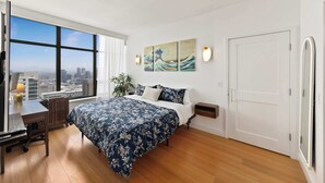 Een slaapkamer met een groot bed, een bureau, een stoel en uitzicht op de stad door grote ramen.