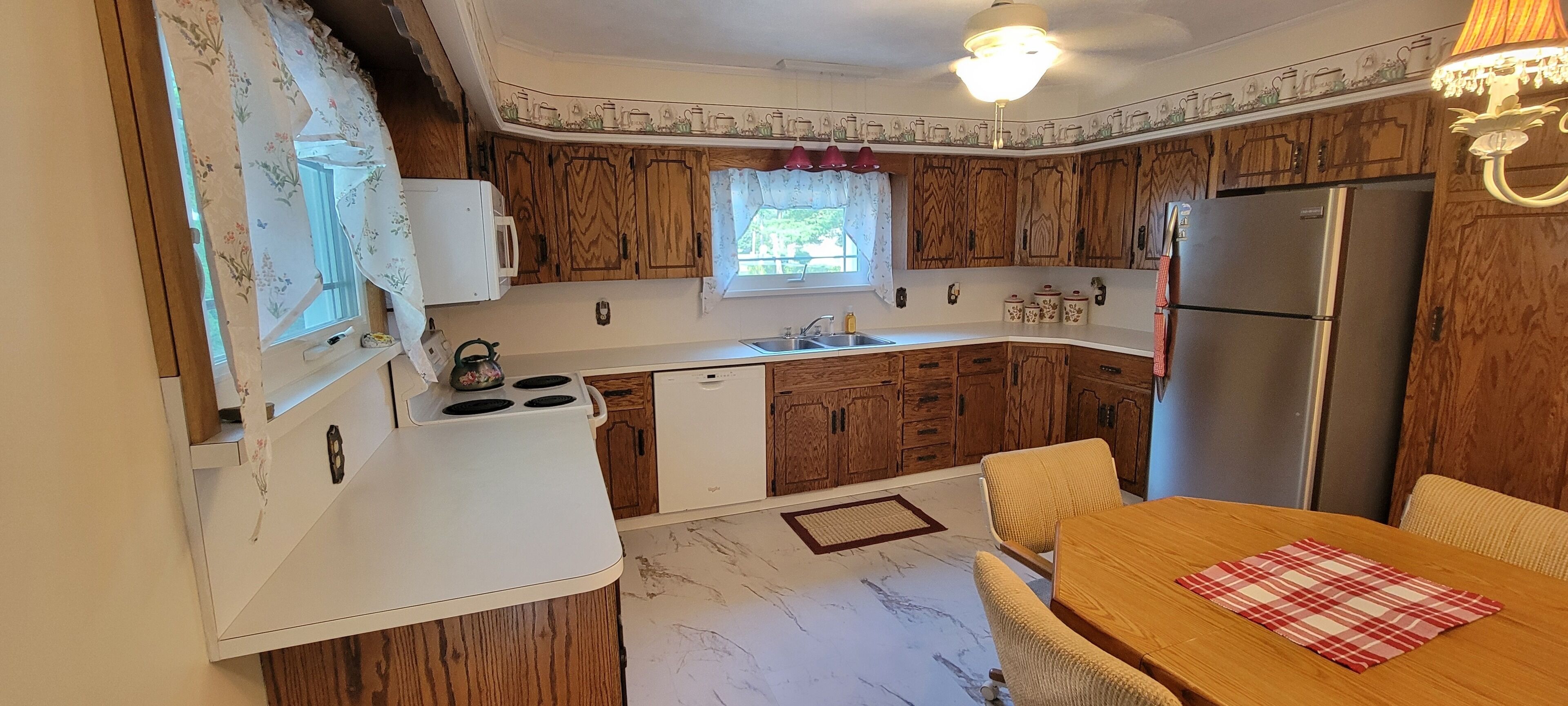 A compact kitchen with wooden cabinets, a white countertop, a stainless steel refrigerator, and a dining area with a table and chairs.