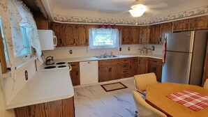 Une cuisine compacte dotée de meubles en bois, d’un plan de travail blanc, d’un réfrigérateur en acier inoxydable et d’un coin repas avec une table et des chaises.