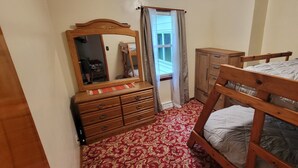Une chambre à coucher avec un lit en bois, une commode à tiroirs, un miroir et une fenêtre avec des rideaux.