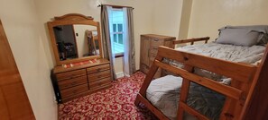 Een slaapkamer met een houten bed, een ladekast, een spiegel en een raam met gordijnen.