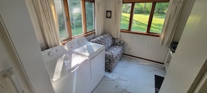 Un cuarto de lavado con lavadora, un sofá estampado y vistas a un jardín verde a través de amplios ventanales.
