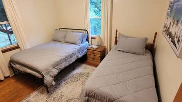 Un dormitorio con dos camas individuales, una mesita de noche con lámpara y una ventana con vistas a árboles.