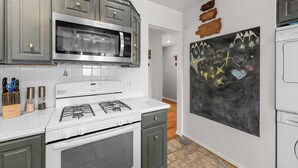 Une cuisine équipée d’une cuisinière à gaz, d’un four à micro-ondes et d’un mur recouvert d’un tableau noir sur lequel est écrit un message de bienvenue.