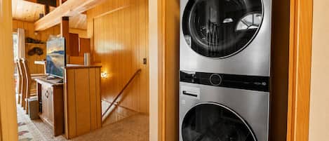 A laundry room with two stacked front-loading washing machines, wooden interior, and a staircase leading to an upper level.