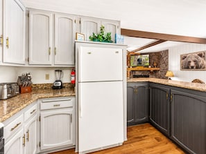 A kitchen with white cabinets, a white refrigerator, granite countertops, and a stone accent wall.