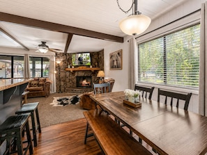 A cozy interior with a stone fireplace, wooden dining table, and large windows.