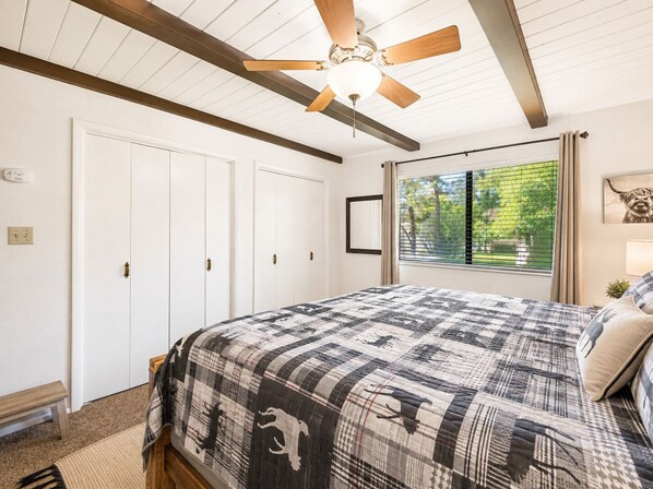A bedroom with a bed, a ceiling fan, a window with blinds, and a door.